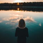 woman wearing black dress standing in front of body of water during sunset